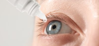 Woman applying eye drops on light background, closeup