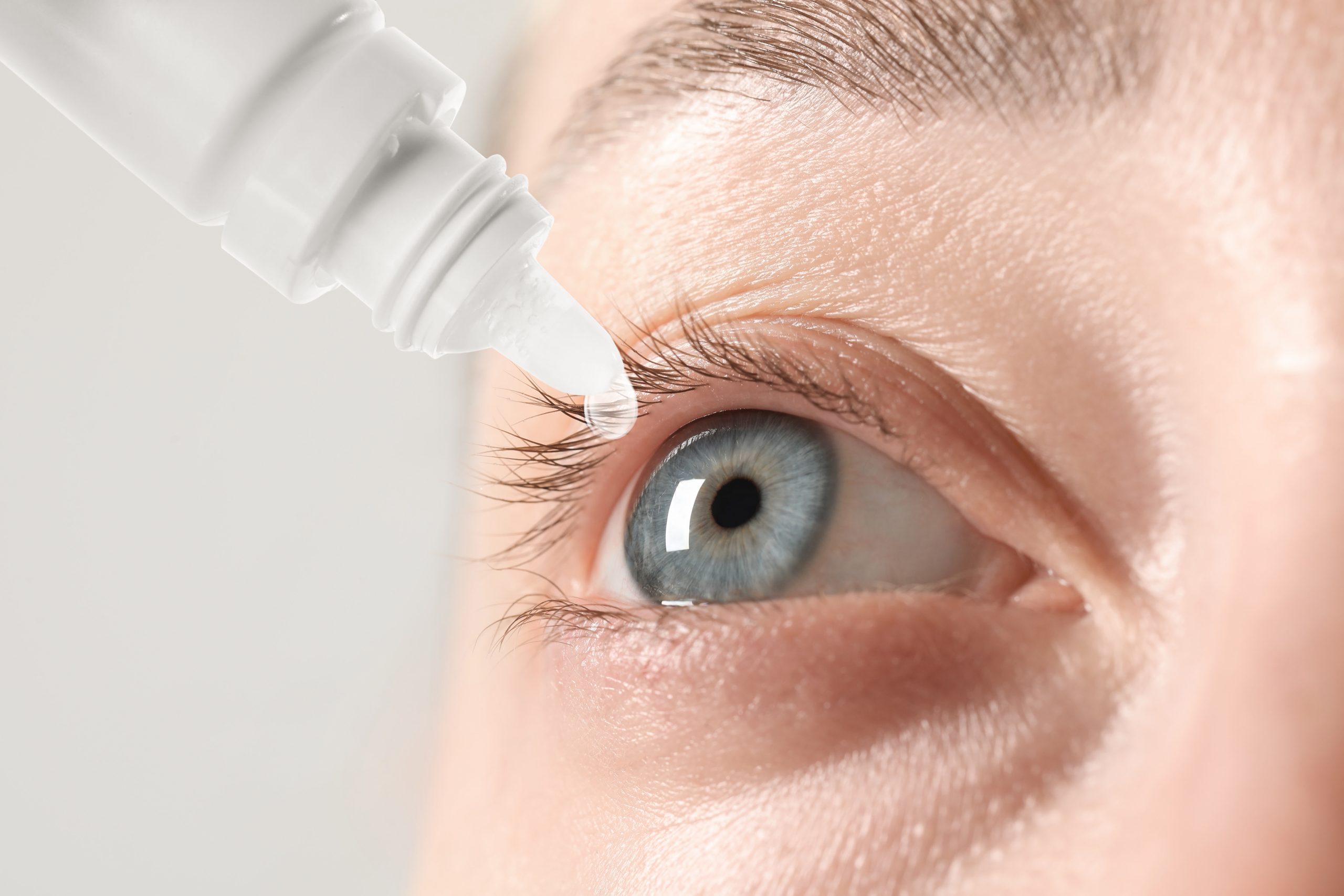 Woman applying eye drops on light background, closeup