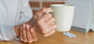 close up senior woman hold on hand to relief shaky symptom while drink water for Parkinson’s disease and chronic illness health care concept