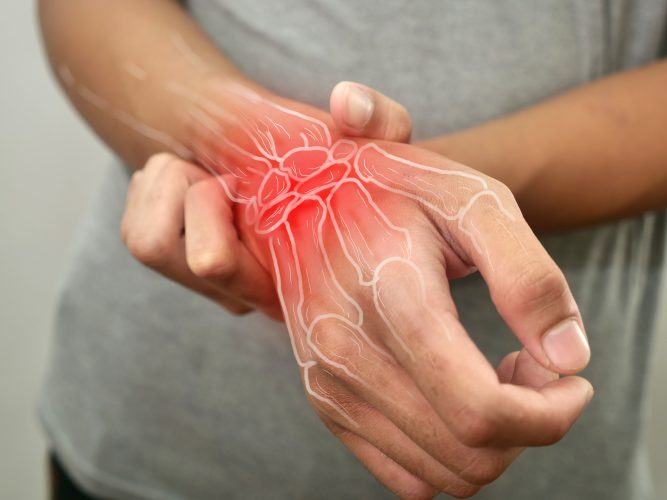 Anonymous person touching his wrist, suferring from arthritis disease, close up against grey background