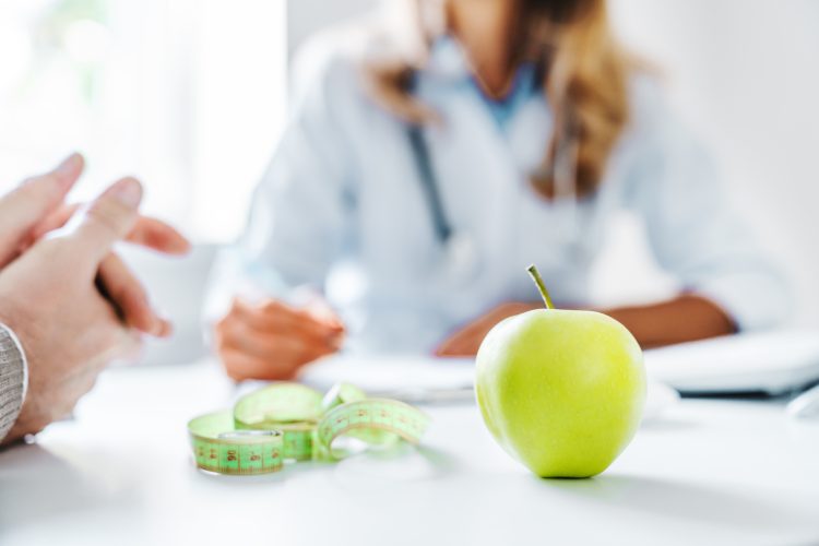 Healthy food concept. Cropped close up of woman doctor dietician recommending senior male patient fresh apple. Weight loss, diet for burning calories. Eating disorder issues
